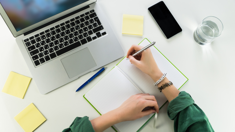 hands writing in notebook on white table