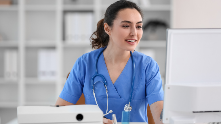 A woman in scrubs sits at a computer