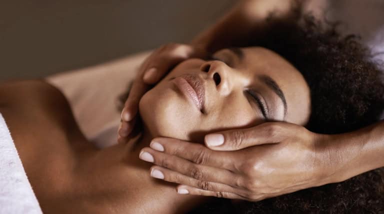 Person receiving a relaxing facial massage with hands gently placed on their face and head.