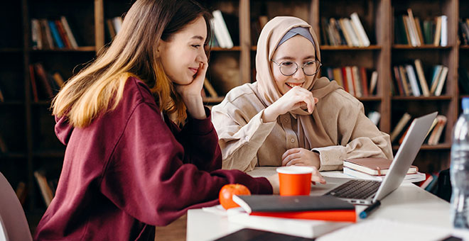 two women smiling around computer