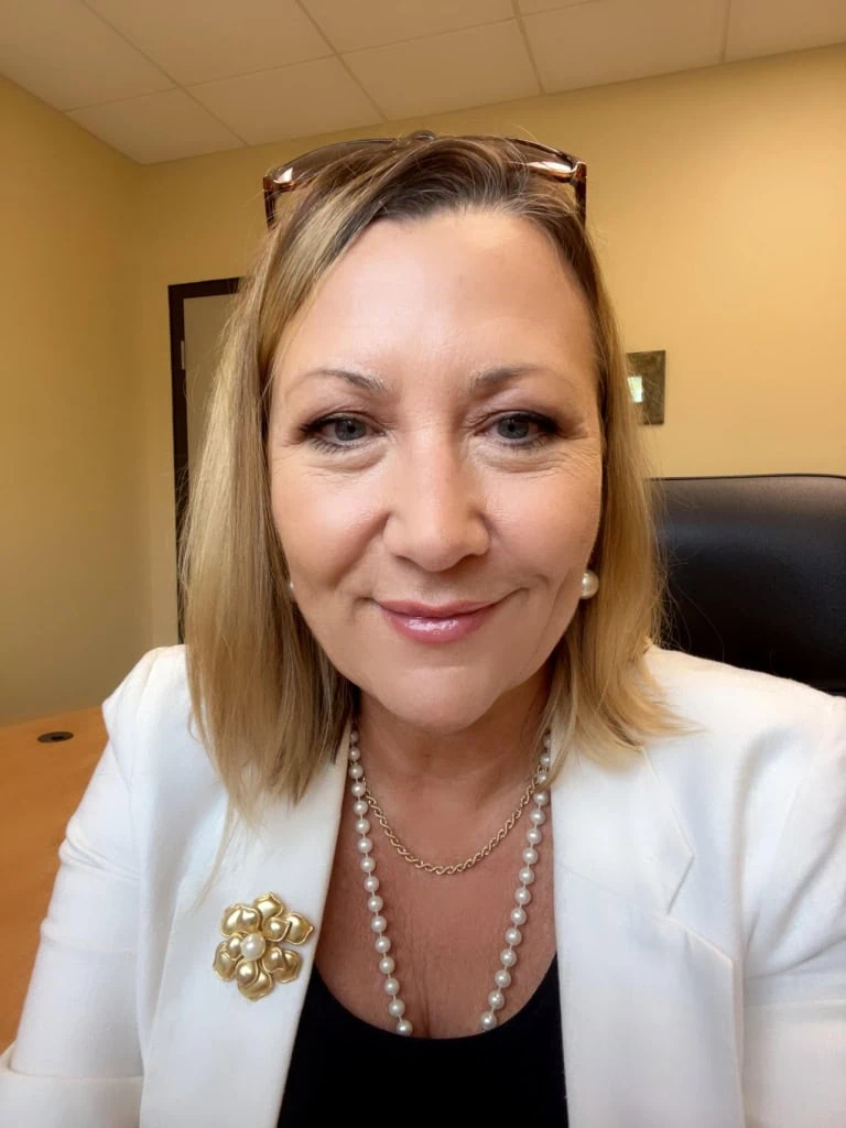 a person in a white blazer and pearls sitting at a desk